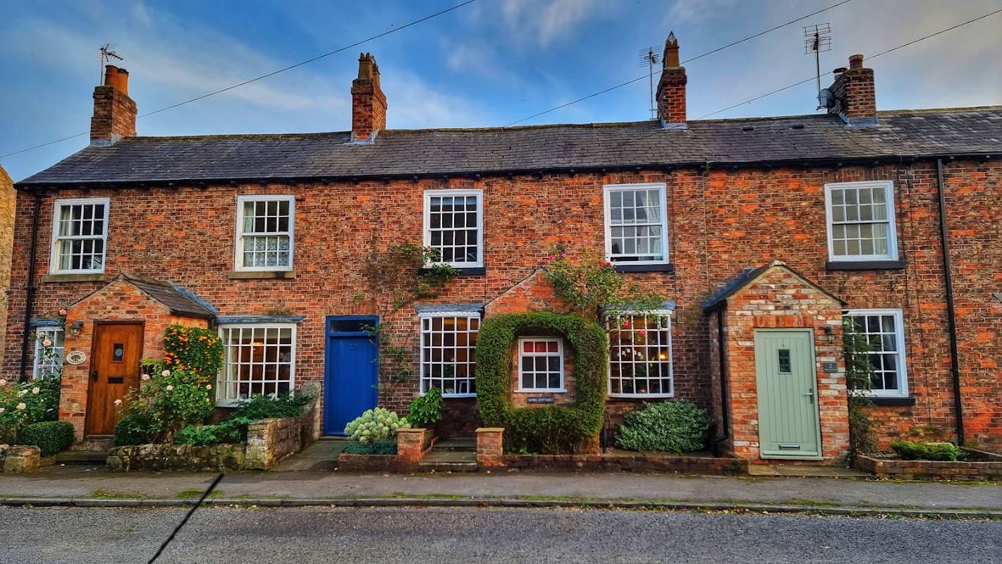 Brick cottages with colorful doors, flower beds, and greenery lining the street in Staveley, Yorkshire.
