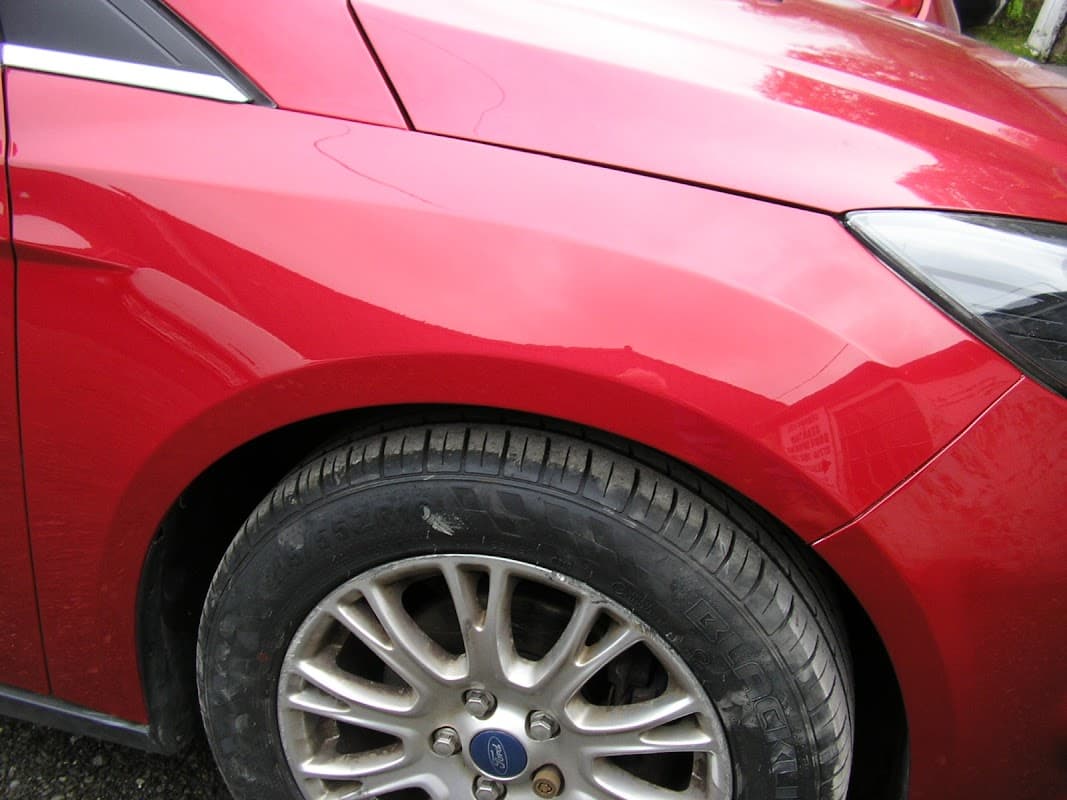 Close-up of a shiny red car's front fender and alloy wheel, showcasing smooth paint and a textured tire.