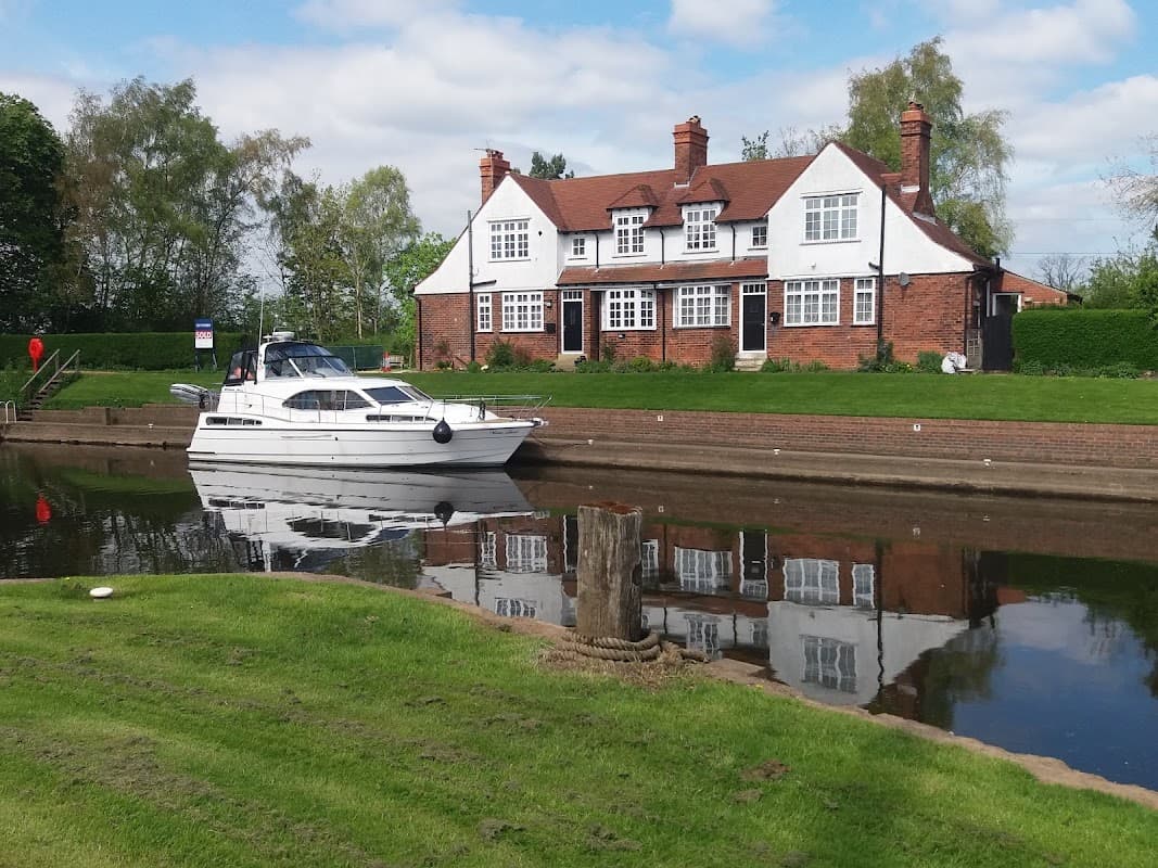 A white boat is moored beside a red-brick building with multiple windows, reflected in the calm water of the canal.