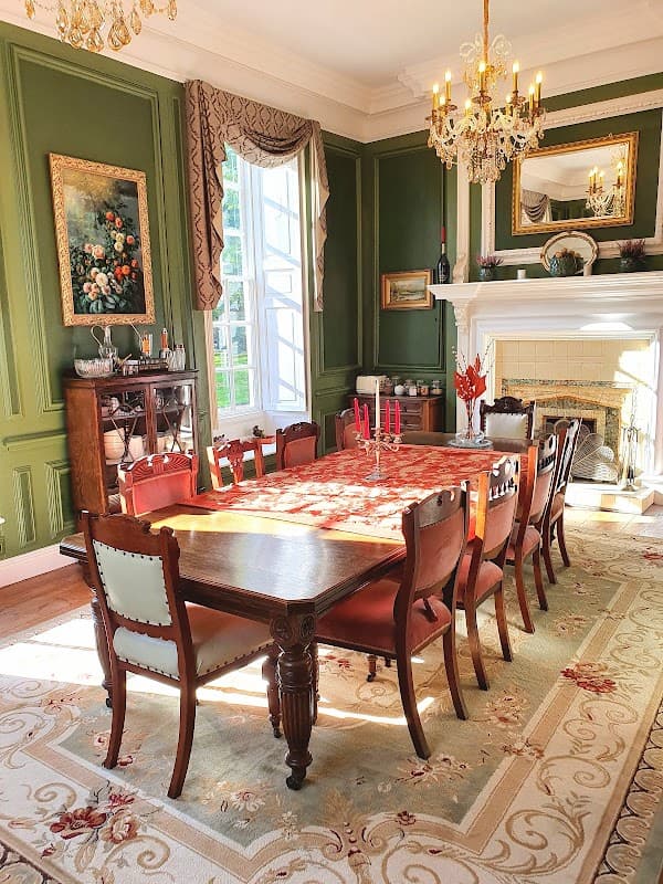 Elegant dining room with a long wooden table, antique chairs, green walls, floral artwork, and a chandelier.