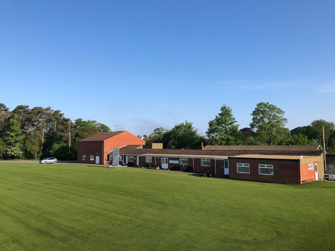 Brick building with a flat roof, surrounded by green grass and trees under a clear blue sky.