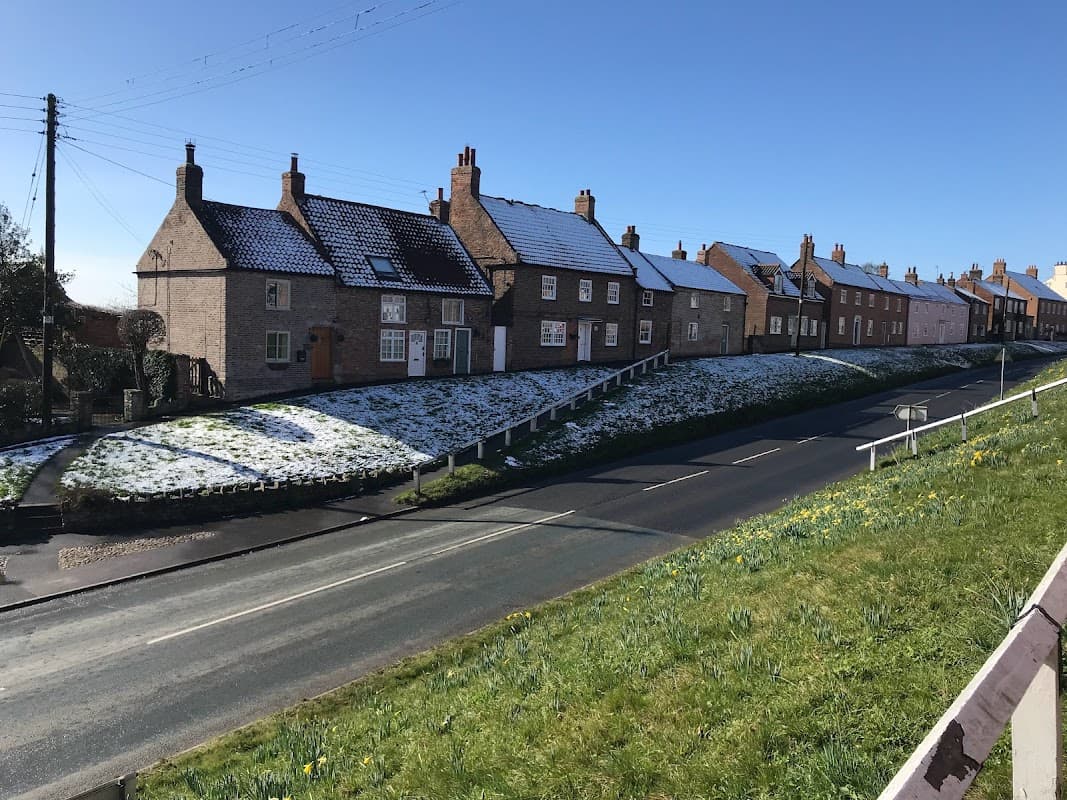 Snow-covered cottages line a quiet street in Stillington, Yorkshire, under a clear blue sky.
