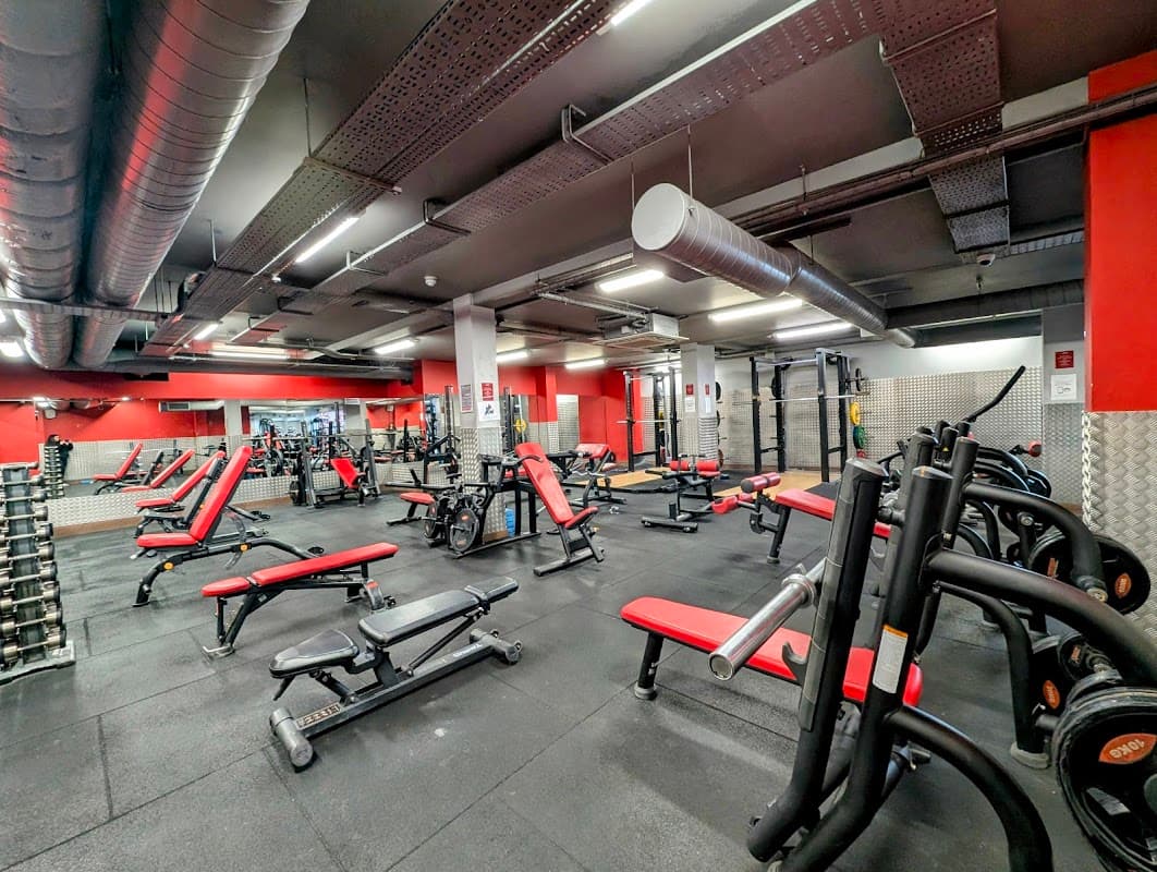 Modern gym interior with red and black equipment, weight benches, and various fitness machines in a spacious layout.