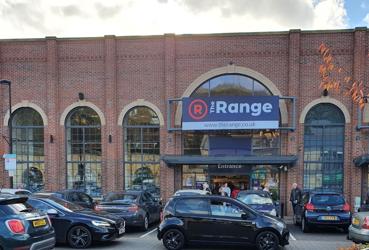 Brick building with large arched windows, featuring a prominent sign for "The Range" and parked cars in front.