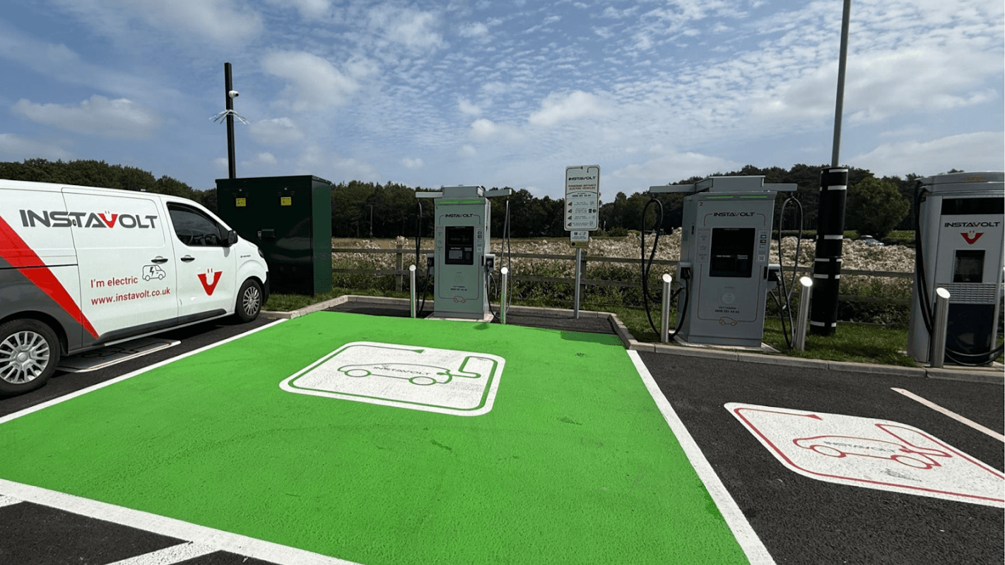 InstaVolt charging station with electric vehicle chargers on green pavement, surrounded by trees and a cloudy sky.