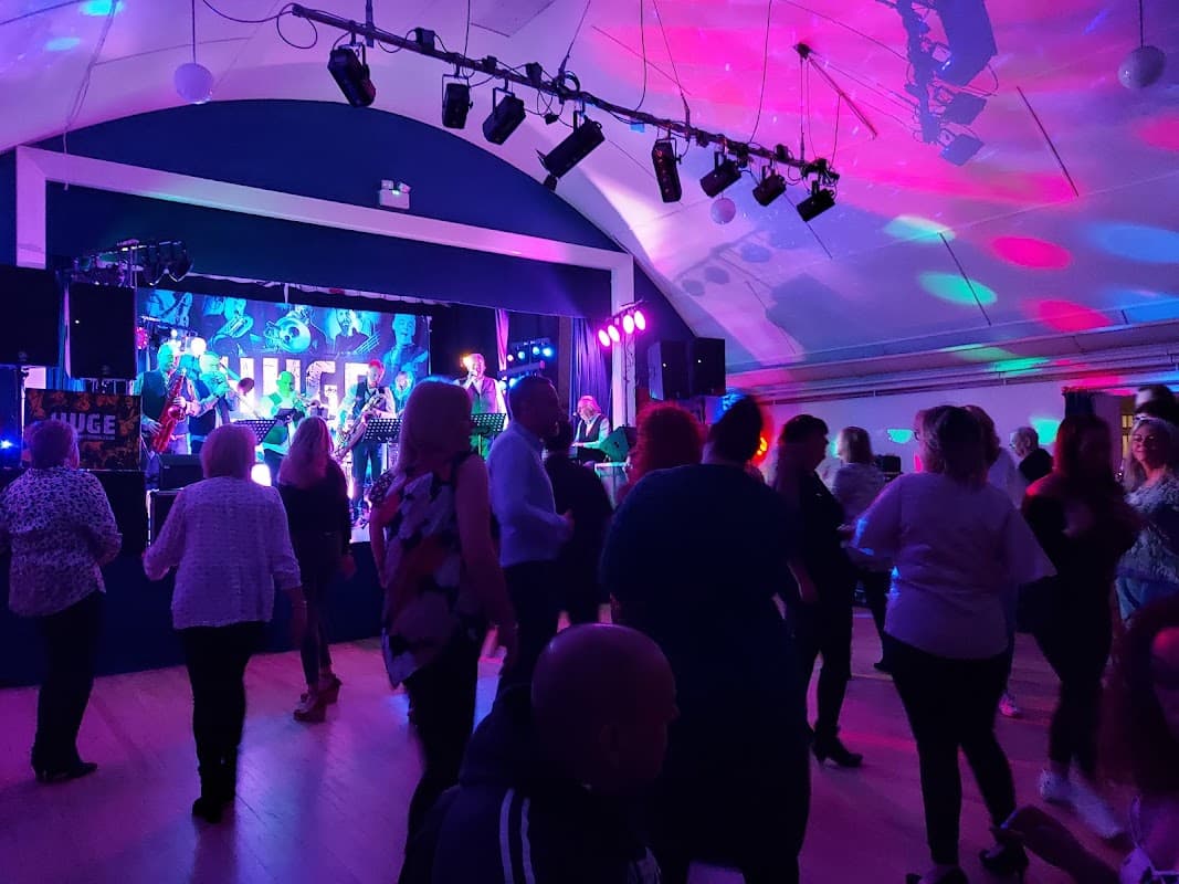 A lively event with people dancing, colorful lights, and a band performing on stage at Stockton on the Forest Village Hall.