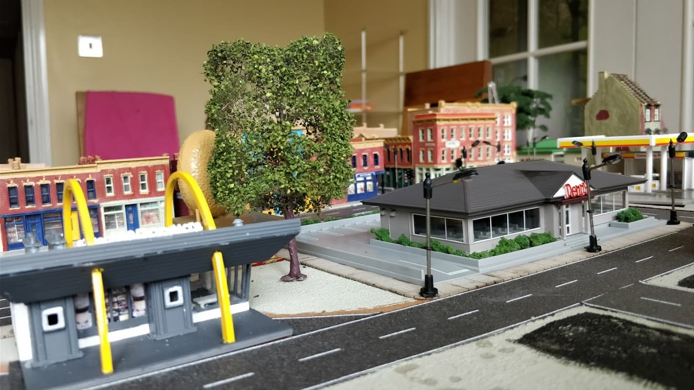 Hobby shop display featuring miniature buildings, trees, and a gas station in a detailed model town setting.