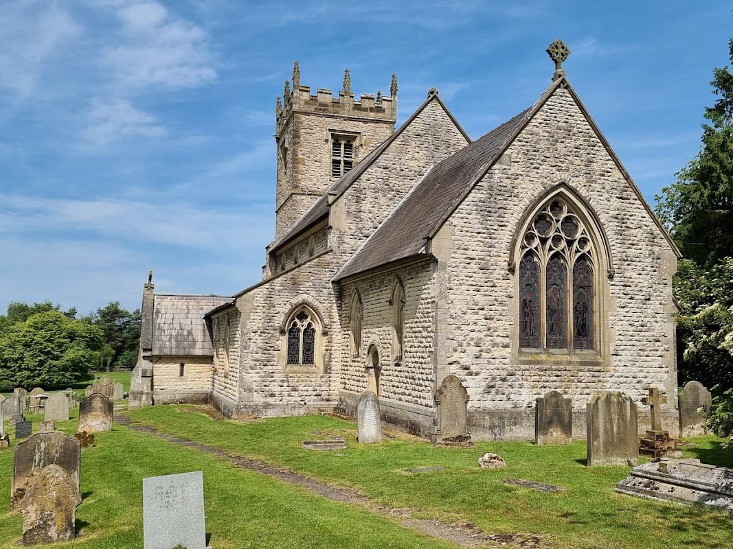 Historic Stonegrave Minster with stone walls, a tower, and a graveyard under a clear blue sky.