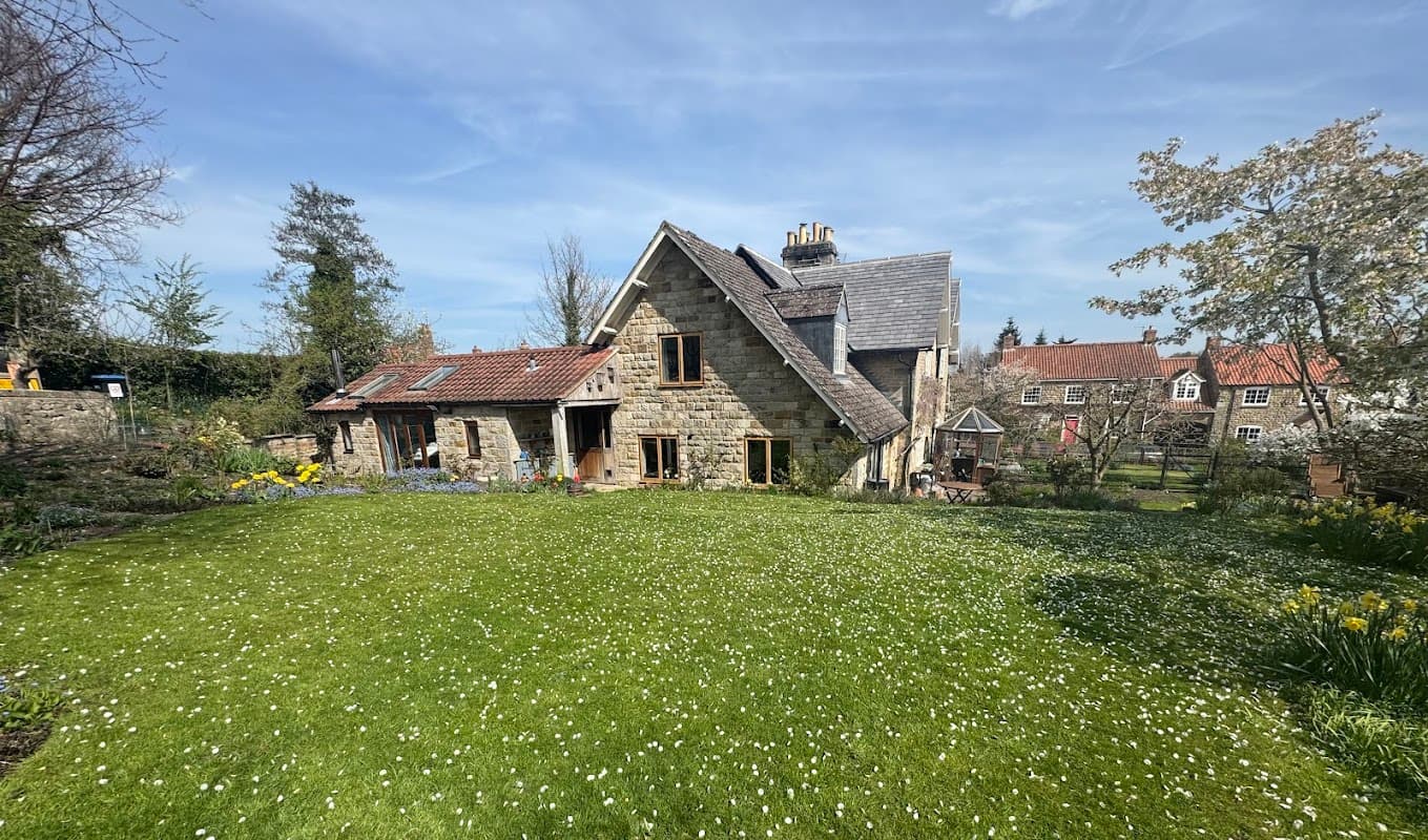 Charming stone hotel with a lush green lawn, colorful flowers, and trees under a clear blue sky in Yorkshire.