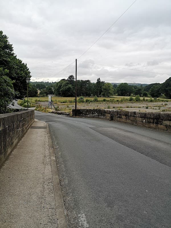 View of a quiet road leading to Summerbridge Stores Ltd, surrounded by greenery and a cloudy sky.