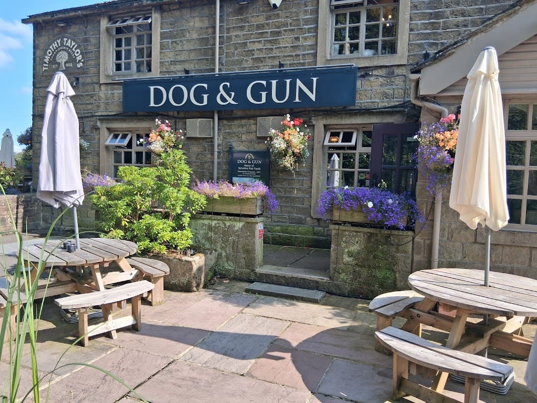 Quaint restaurant exterior with "DOG & GUN" sign, flower pots, outdoor seating, and umbrellas in Sutton-in-Craven.