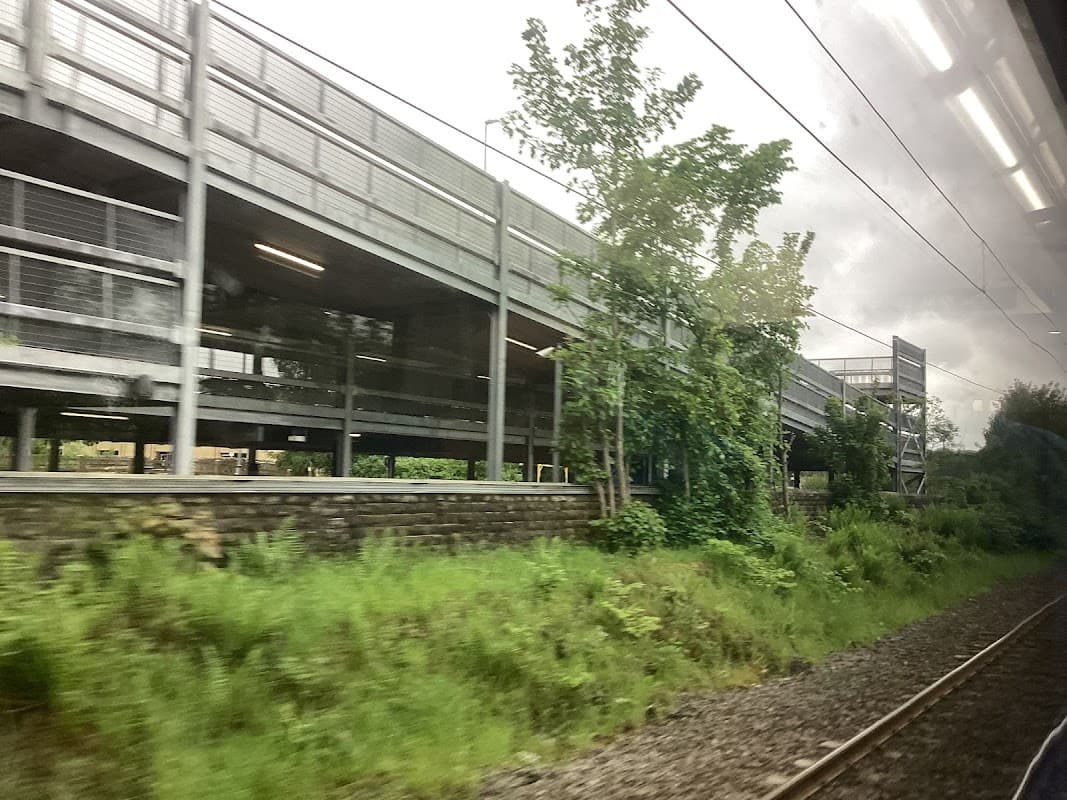 Multi-level car park surrounded by greenery and railway tracks under a cloudy sky in Sutton-in-Craven, Yorkshire.