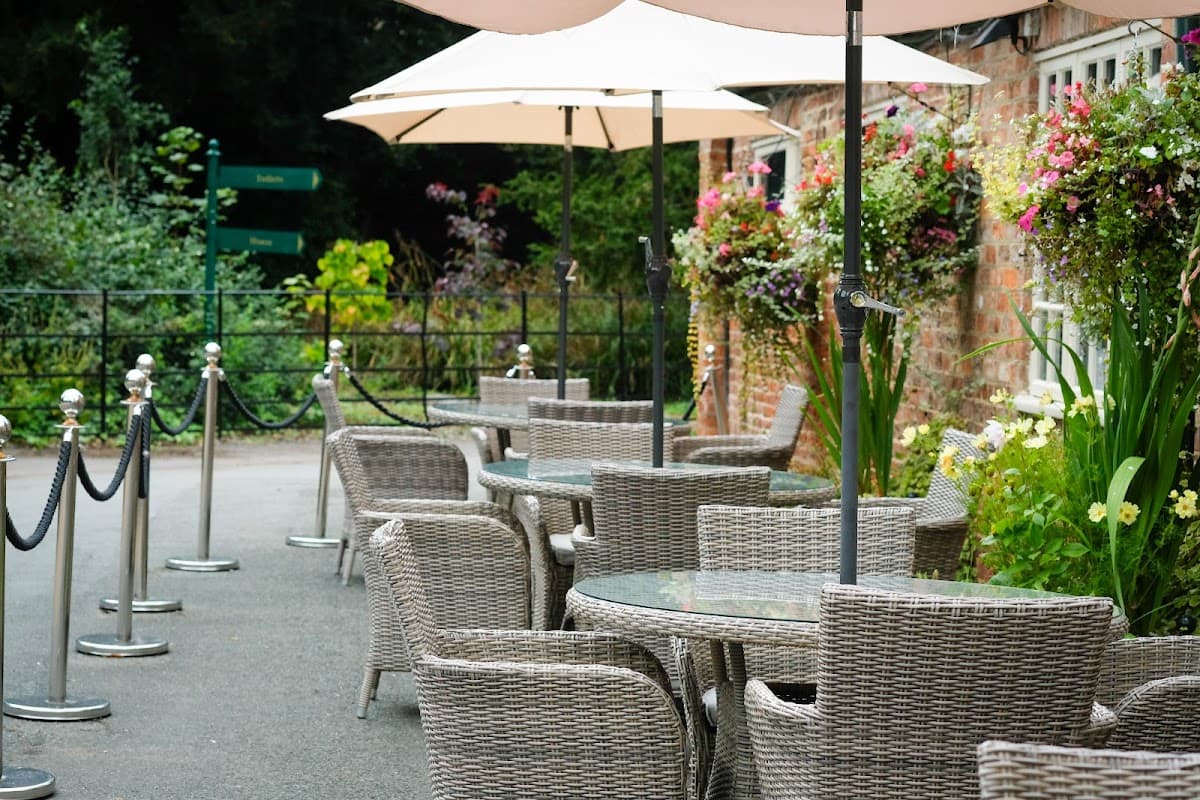 Outdoor seating area at Miss Daisy's Tea Rooms with wicker chairs, tables, and umbrellas, surrounded by flowers.