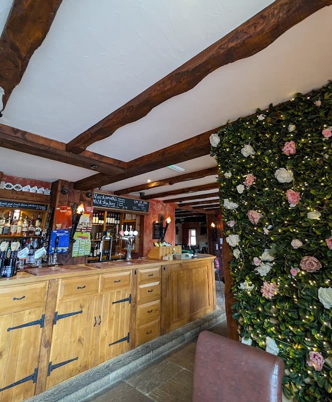 Rustic bar interior with wooden beams, a wooden counter, and a floral wall feature adorned with pink and white flowers.