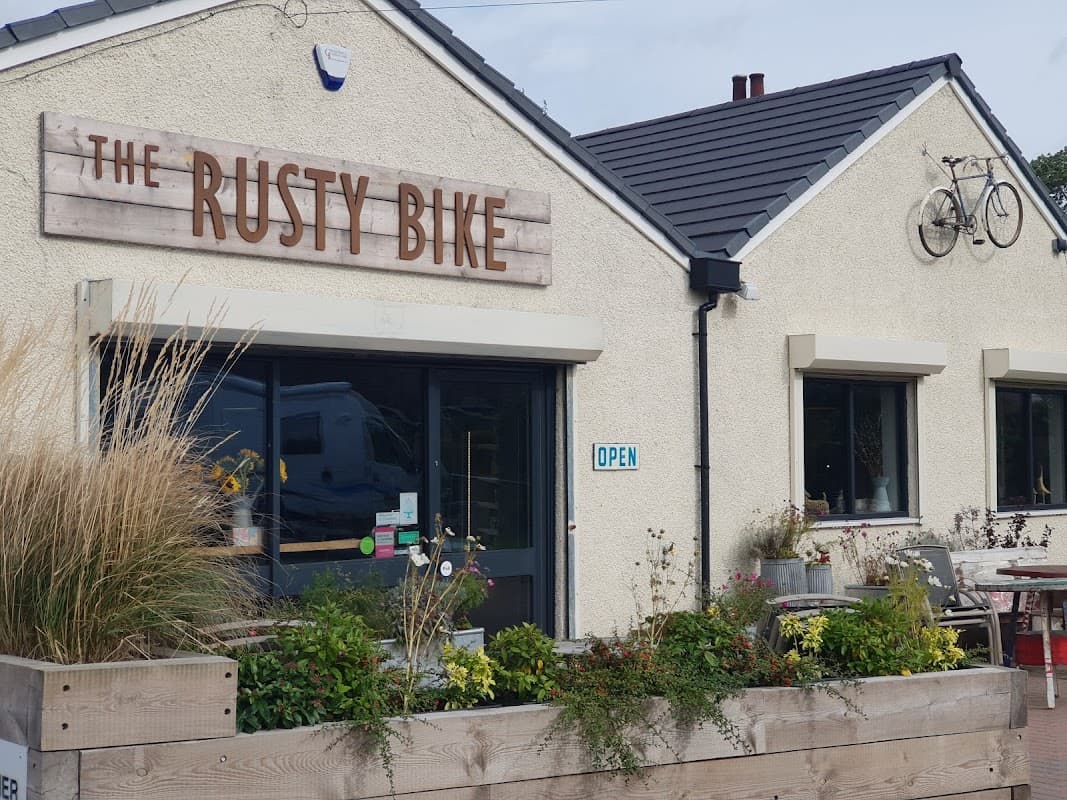 Rusty Bike Cafe exterior with wooden sign, open door, bicycle decoration, and planters with greenery.