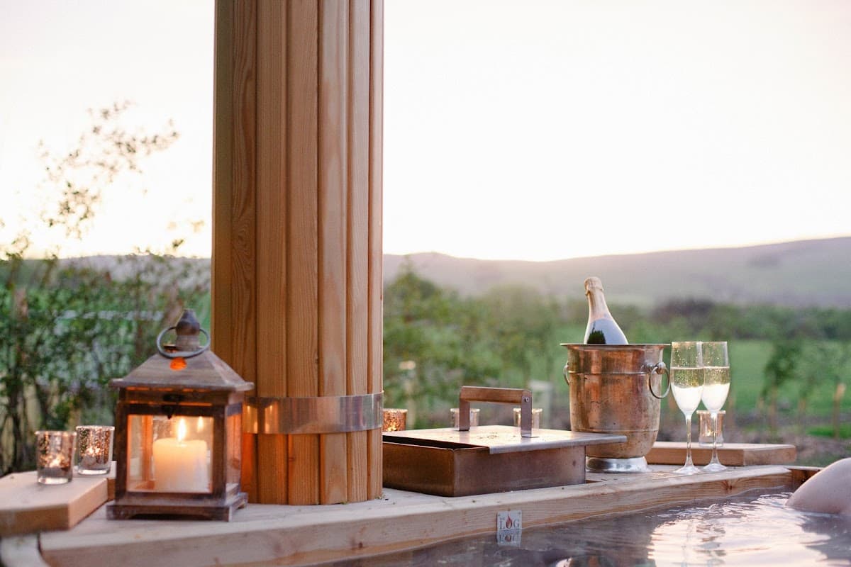 Relaxing outdoor hot tub scene with champagne, glasses, lantern, and scenic Yorkshire countryside at sunset.
