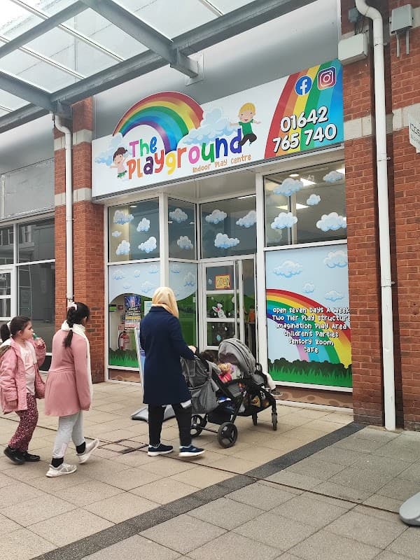Brightly colored entrance to "The Playground" with children and adults walking by, featuring a rainbow and clouds in the design.