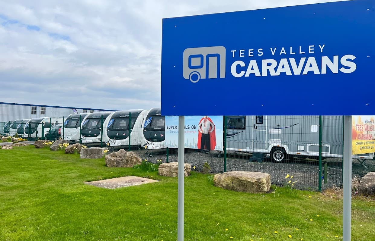 Sign for Tees Valley Caravans Ltd outside a shop showcasing multiple caravans on display in a grassy area.