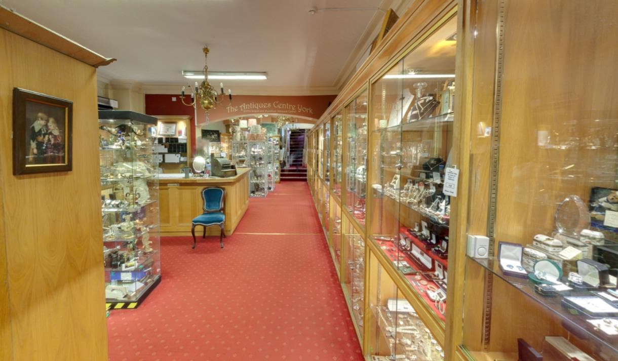 Elegant antiques showroom with glass display cases, red carpet, chandelier, and vintage furniture, creating a classic atmosphere.