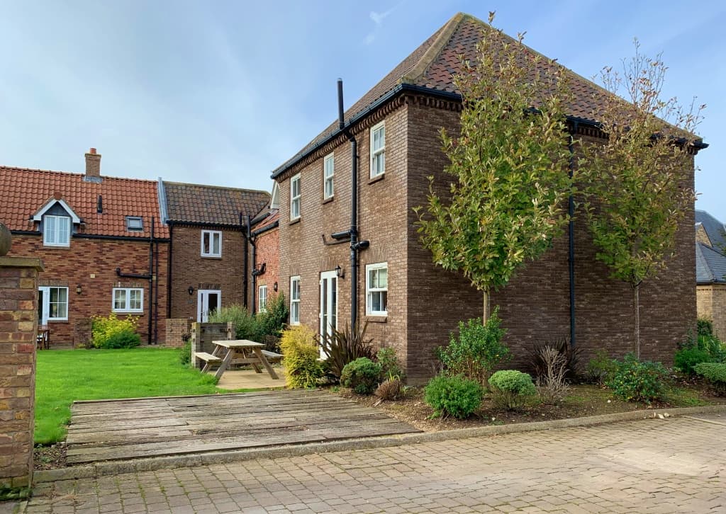 Two-story brown brick building with a garden, picnic table, and greenery in a residential area of Filey, Yorkshire.