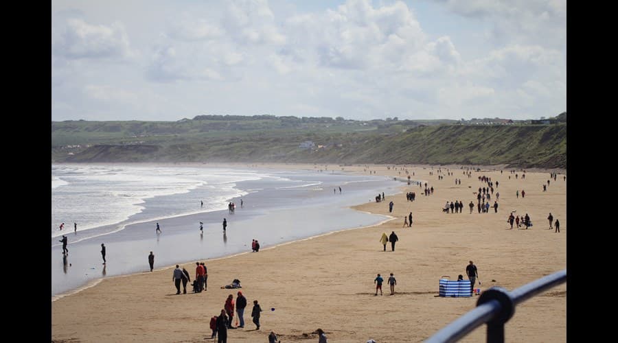 Crowded sandy beach with waves, cliffs in the background, and people enjoying the seaside at Filey, Yorkshire.