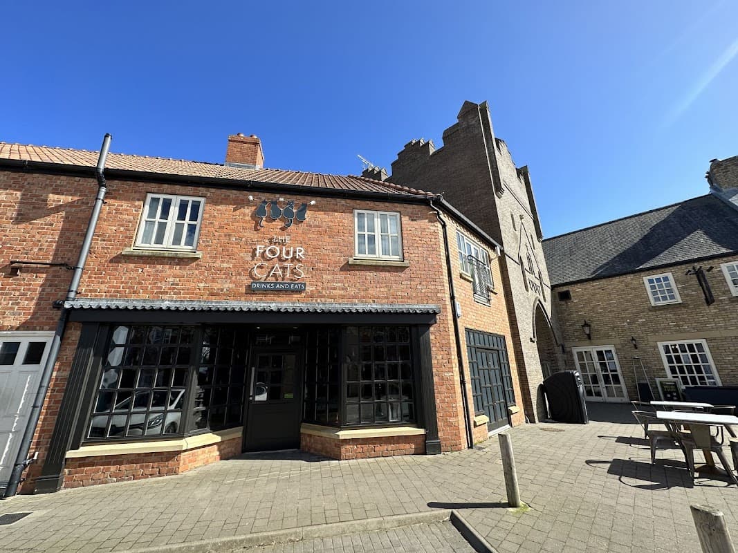 Red brick building with large windows, sign reading "Four Cats" and outdoor seating area under a clear blue sky.
