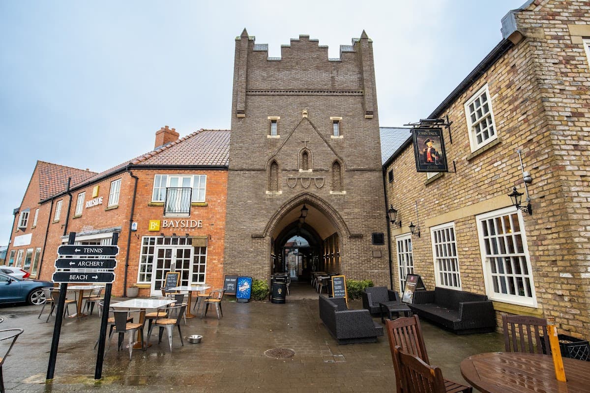 Meadowside House with a stone archway, shops, and outdoor seating in a coastal town setting.