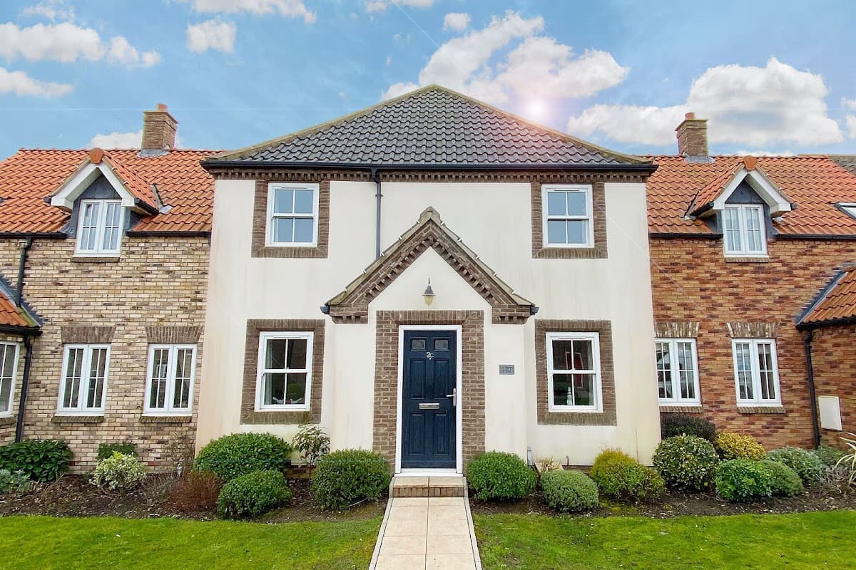 Charming two-story building with a dark door and white facade, surrounded by well-maintained gardens and blue sky.