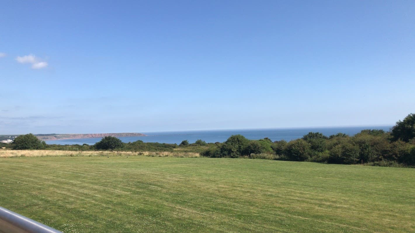 Vast green field overlooking a serene blue sea and distant cliffs under a clear blue sky in Filey, Yorkshire.