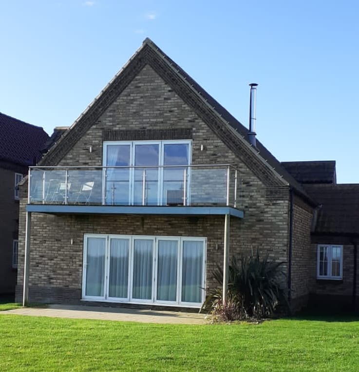 Modern brick house with a balcony, large windows, and green lawn under a clear blue sky.