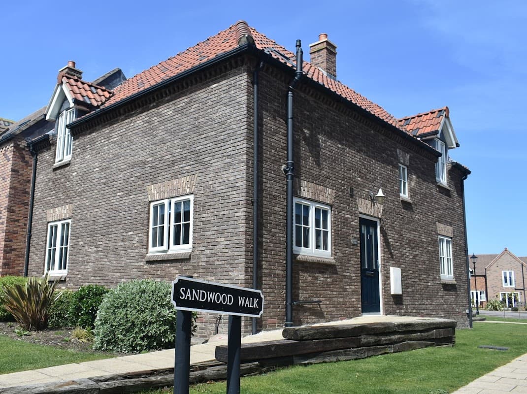 A brick house with a dark door and white windows, surrounded by green grass and a sign for Sandwood Walk.