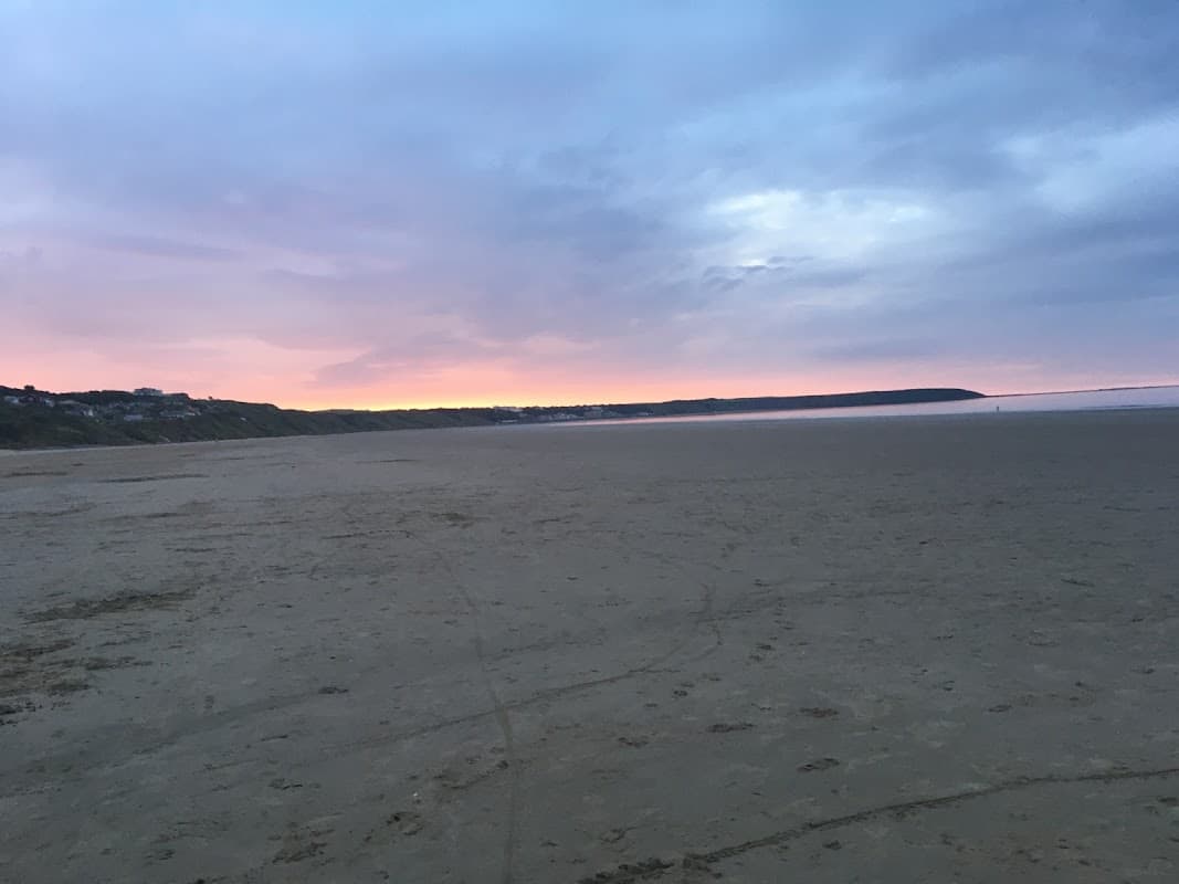 Serene beach at sunrise with soft pastel colors in the sky and distant cliffs along the coastline in The Bay, Filey.