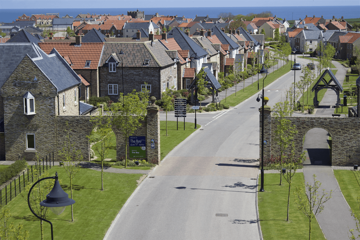 Quaint residential area in The Bay Filey, featuring stone houses, manicured lawns, and a clear blue sky.