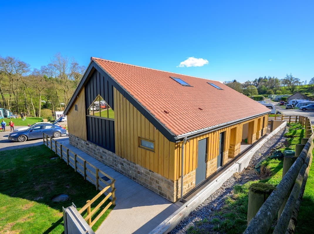 Modern wooden holiday cottage with a sloped roof, surrounded by greenery and a clear blue sky in North Yorkshire.