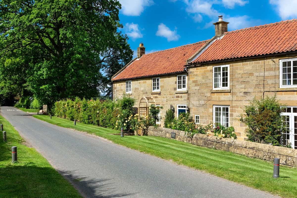Charming stone building with red roof, surrounded by greenery, along a quiet road in North Yorkshire. Bright blue sky.