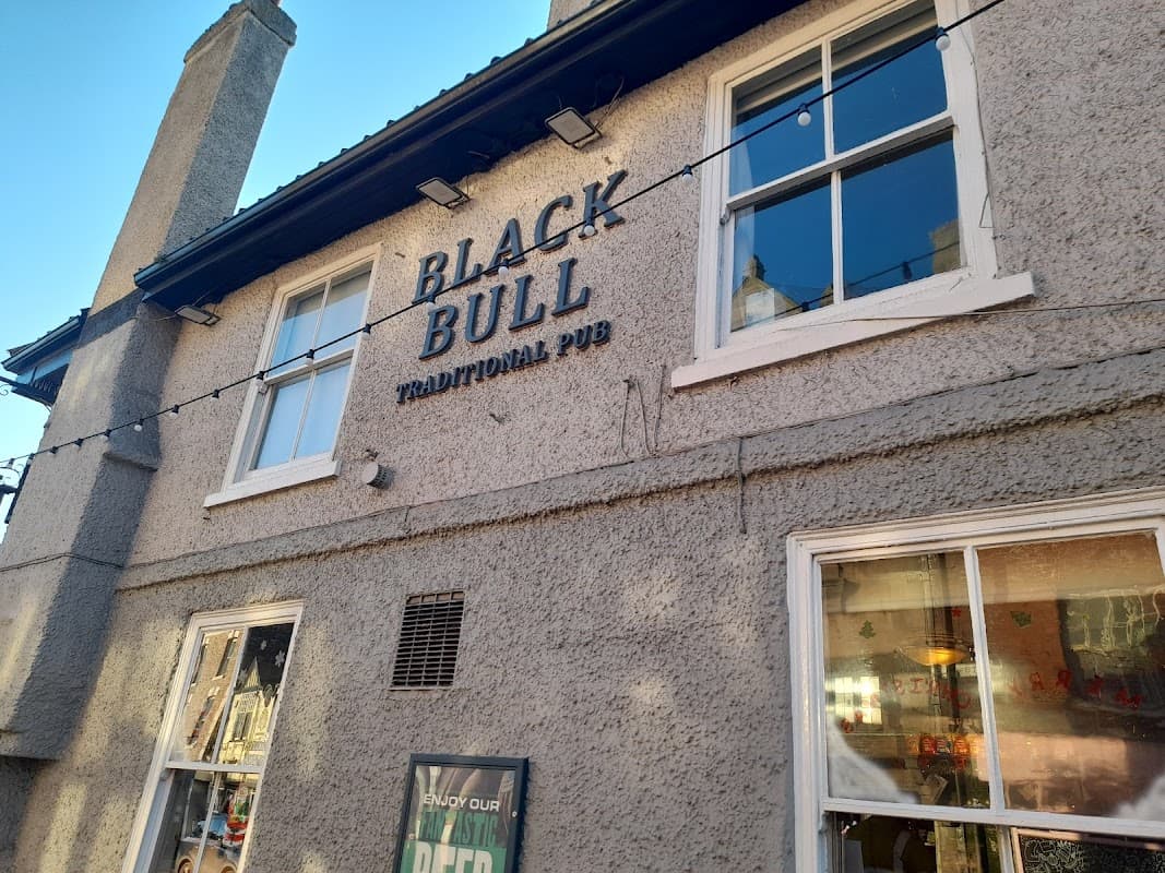 Exterior of the Black Bull pub in Thirsk, featuring a sign and large windows under a clear blue sky.