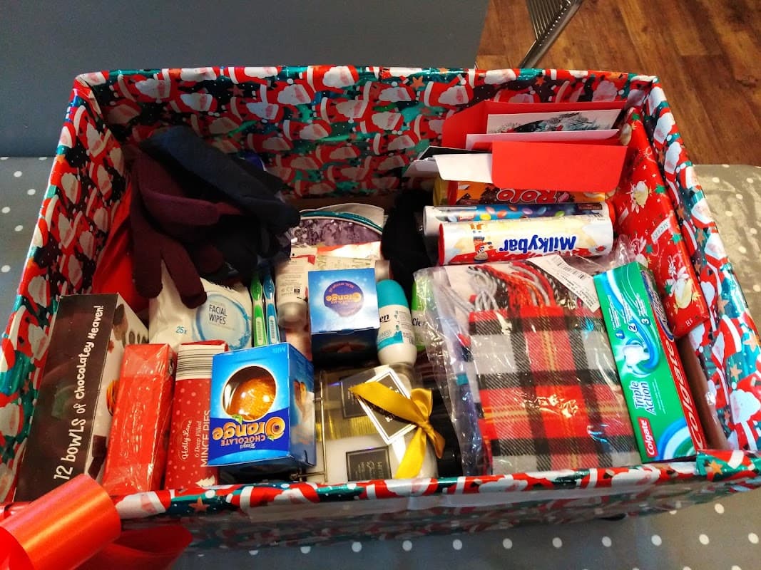 A festive box filled with various gifts, including chocolates, toiletries, and a plaid scarf.