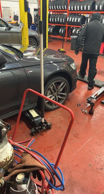 Kwik Fit shop interior with a car on a lift, mechanic working, and tire racks in the background.