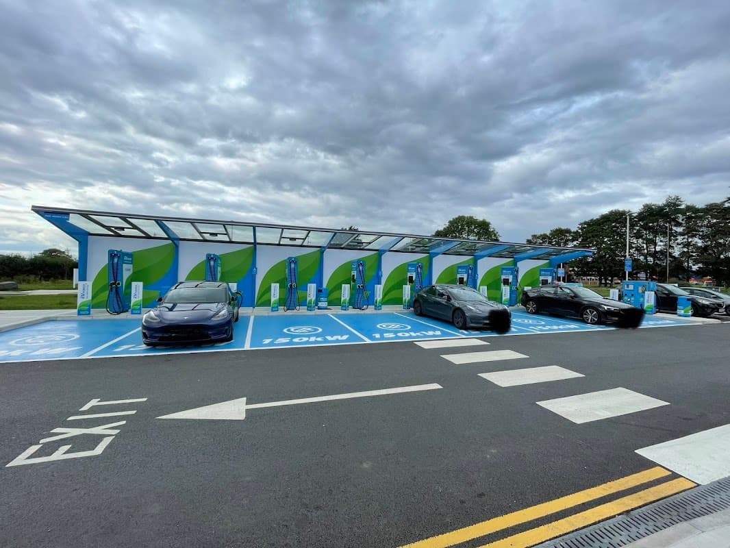 MFG Charging Station with multiple electric vehicle chargers and parked cars under a cloudy sky in Thirsk, Yorkshire.