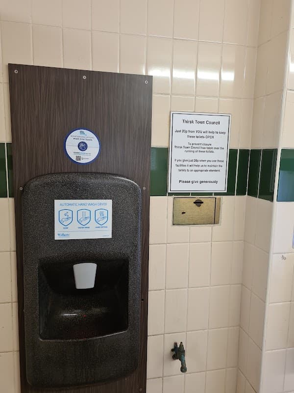Automatic hand dryer mounted on a wall, with a sign about maintaining public toilets in Thirsk, Yorkshire.