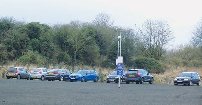 Cars parked in a gravel lot with trees in the background, featuring a sign for Station Road Car Park.