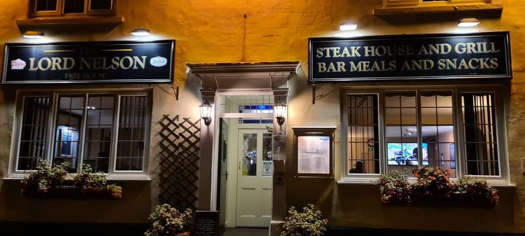 The Lord Nelson pub entrance with signage for steak house, grill, and bar meals, surrounded by flower boxes.