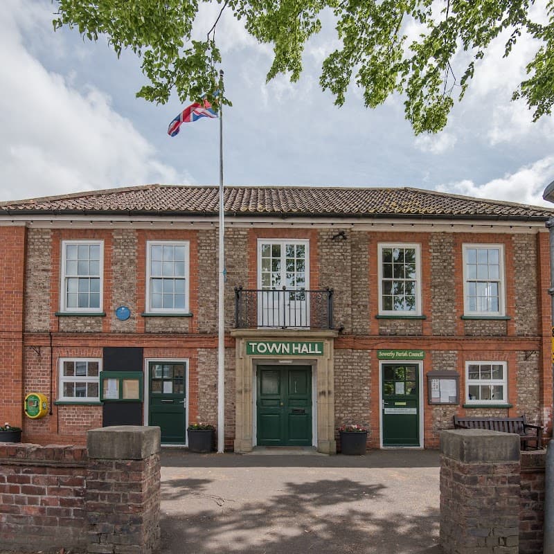 Brick building with green doors, a flagpole, and large windows, featuring a sign that reads "TOWN HALL."