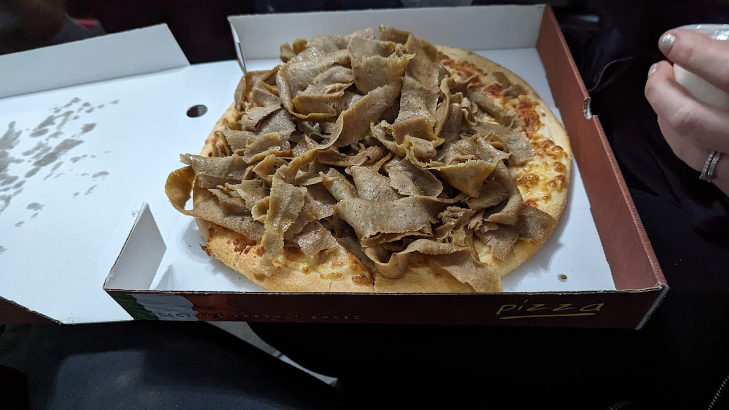 Pizza topped with a generous layer of sliced meat, served in a takeout box from Farooqs Thornaby restaurant.