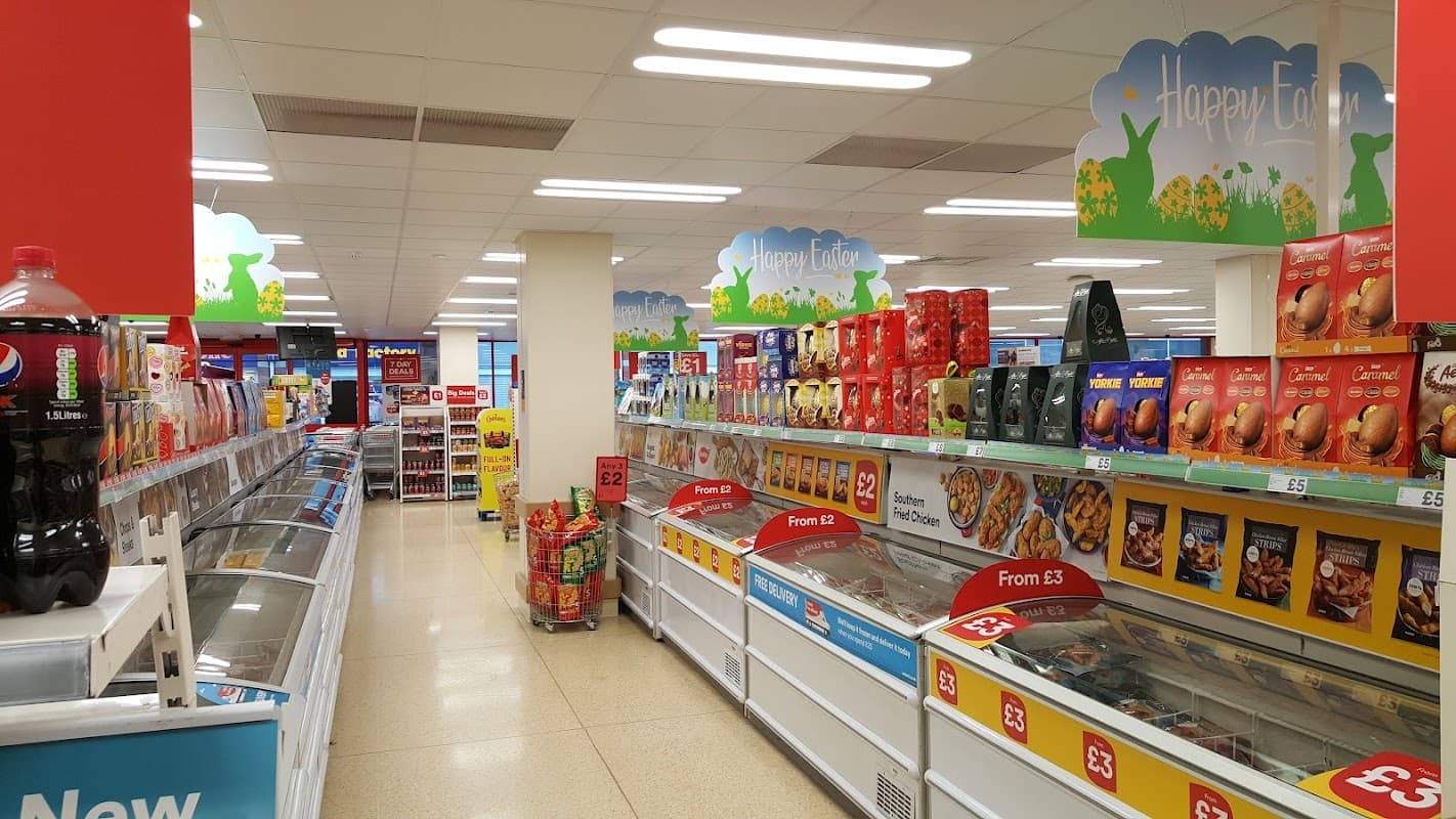 Bright supermarket aisle with freezers, snacks, and drinks, featuring colorful signage and promotional displays.
