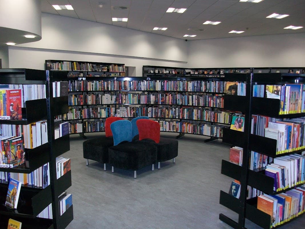 Bookshelves filled with books surround a cozy seating area with blue and red chairs in a modern library interior.