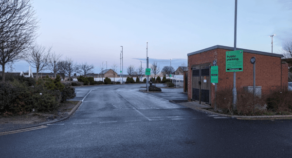 Public parking area in Thornaby, Yorkshire, featuring a brick building, signage, and surrounding trees.