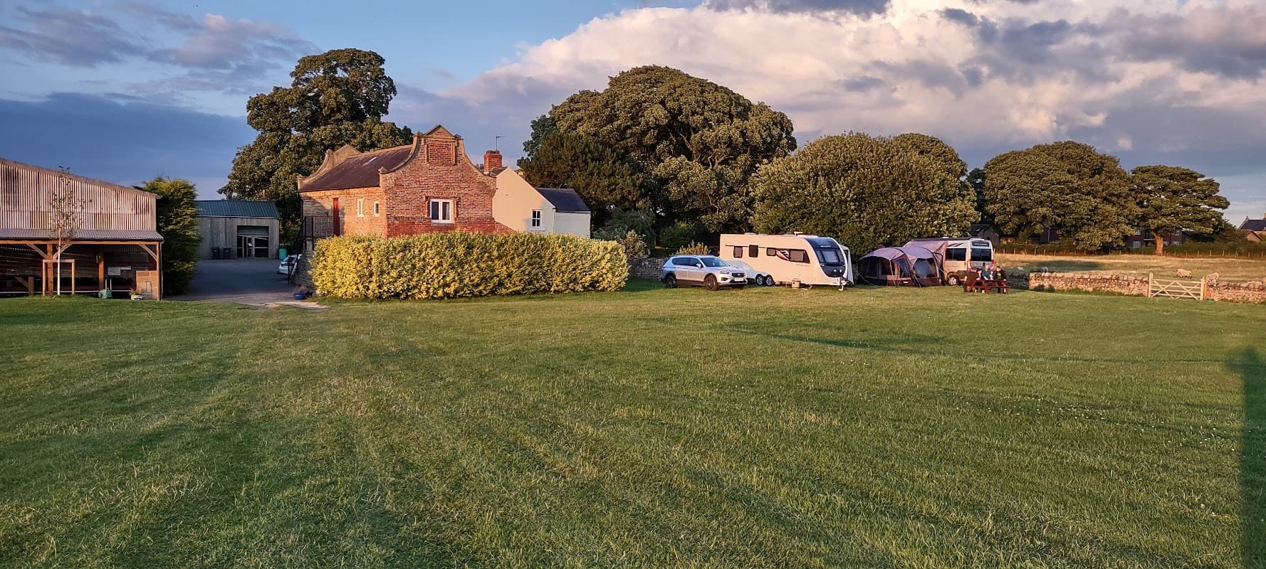 Caravan park with grassy area, parked caravans, and a brick building under a partly cloudy sky in Thornborough, North Yorkshire.