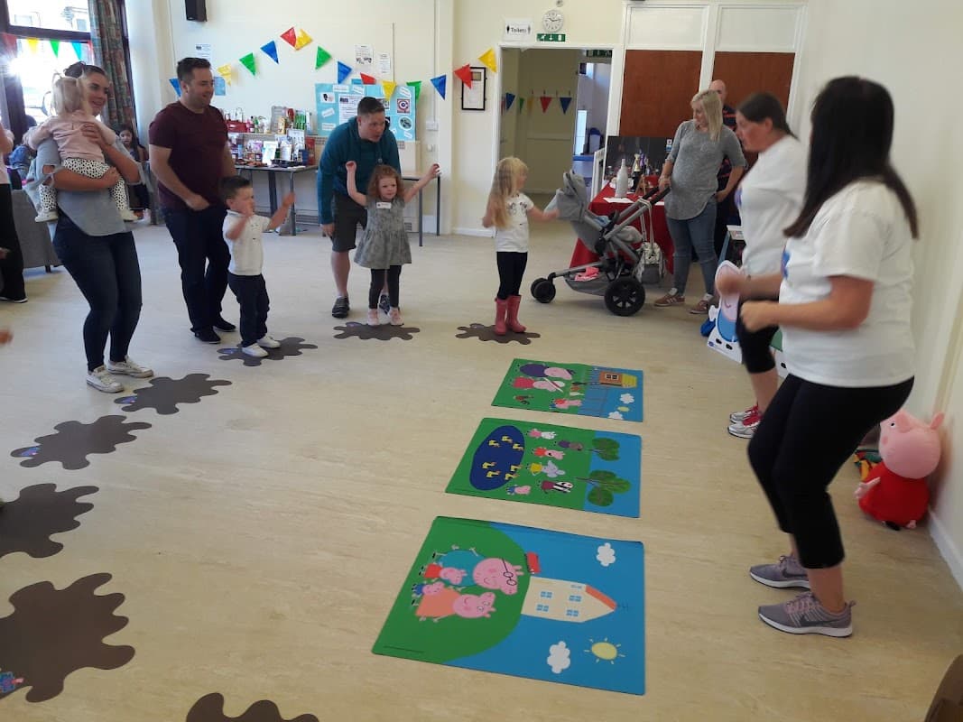 Children and adults participate in activities on colorful mats, with decorations and a playful atmosphere in a community center.