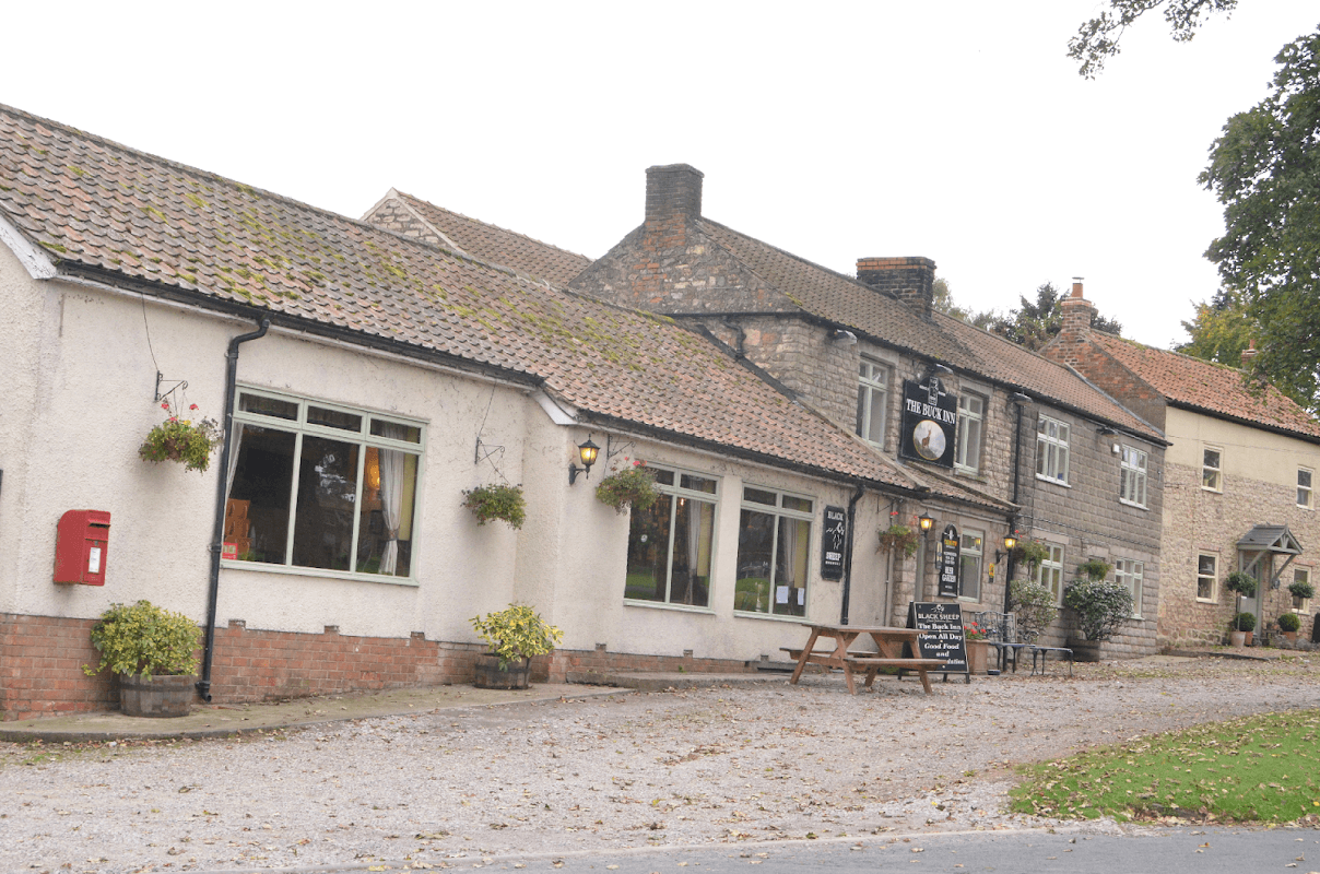 Charming Bed & Breakfast with stone and brick exterior, outdoor seating, and flower baskets in a quaint Yorkshire village.